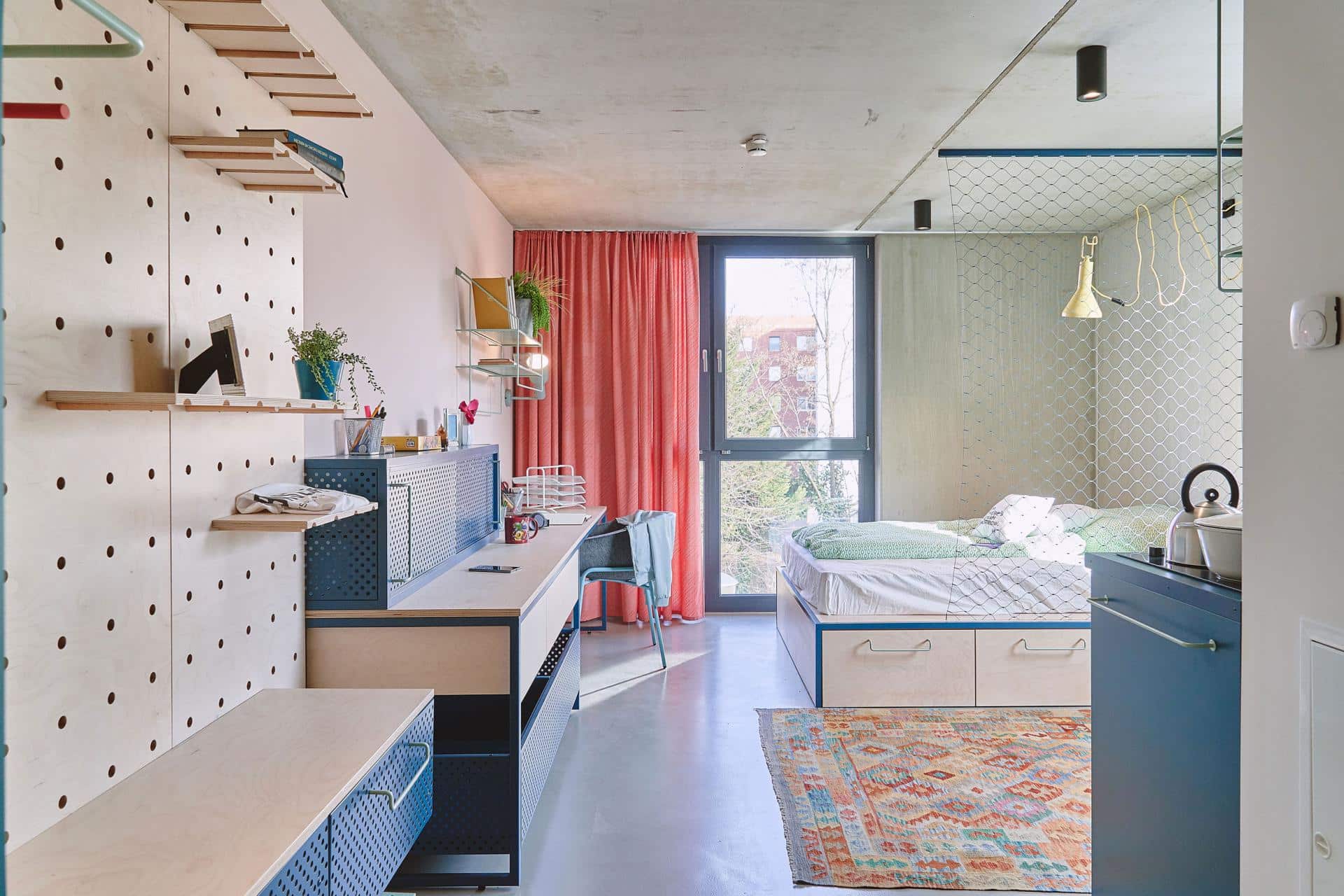 bed and study area of a studio room with kitchenette at Basecamp Leipzig student accommodation