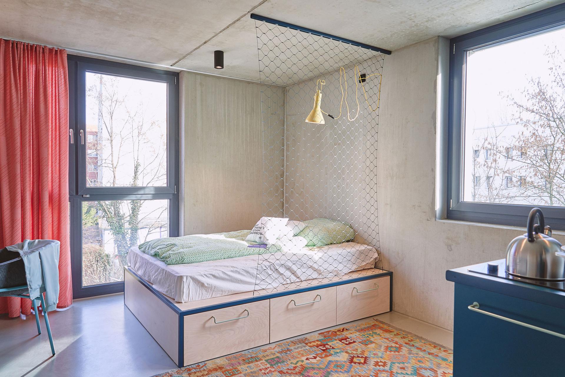 bed and large windows in a studio room with kitchenette at Basecamp Leipzig student accommodation