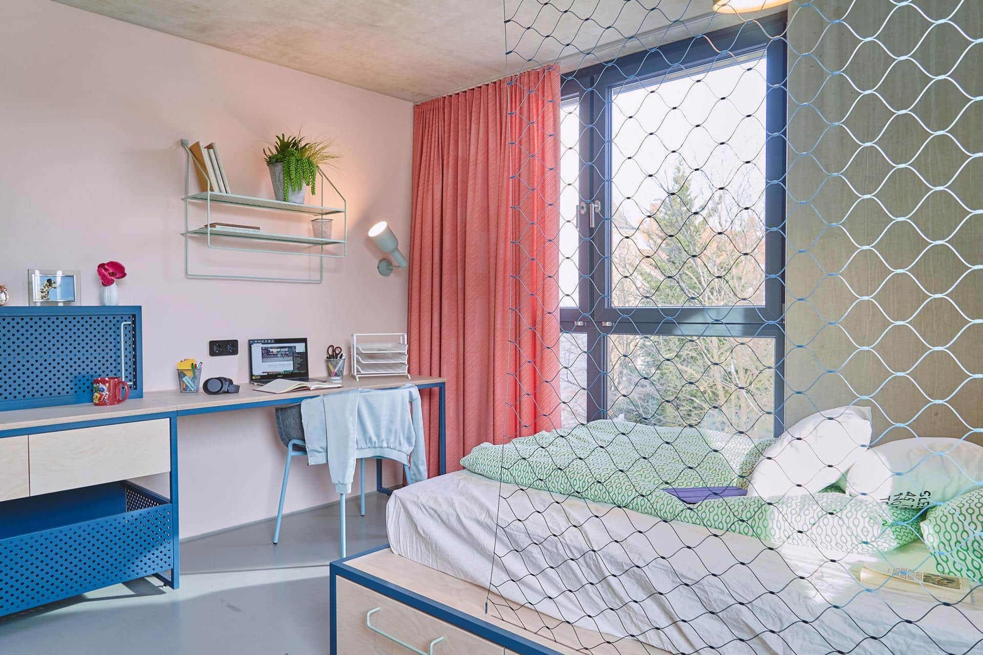 Bed and study area of a studio room with kitchenette at Basecamp Leipzig student housing