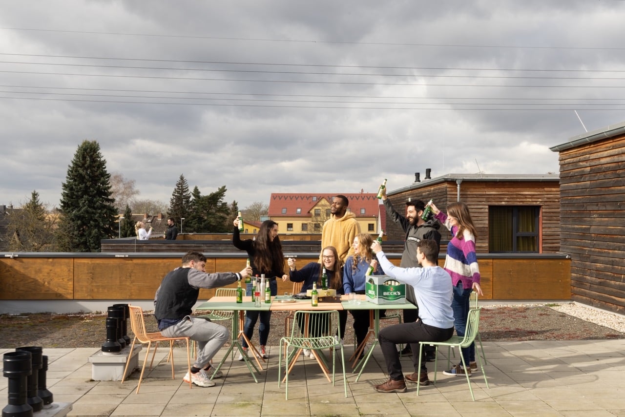 A group of guests living at Basecamp Potsdam dorm celebrate with a beer at the roof terrace area