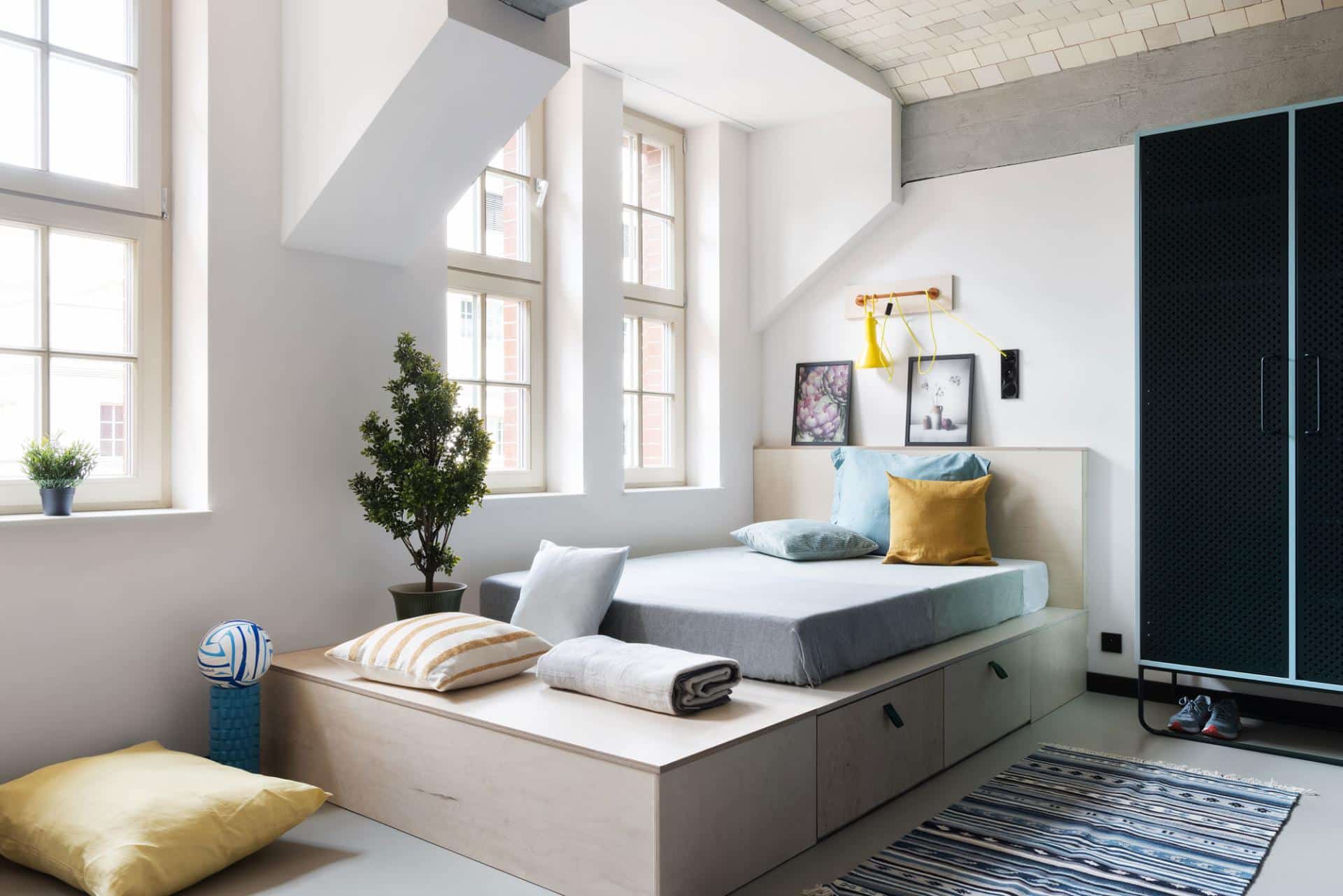 Bed area with large windows and colourful pillows in single room at Basecamp Wroclaw dorm