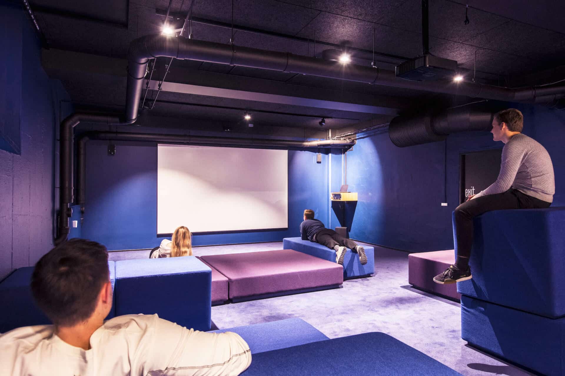 Four students relax on the sofas of the cinema room at Basecampa Copenhagen South Campus student dormitory