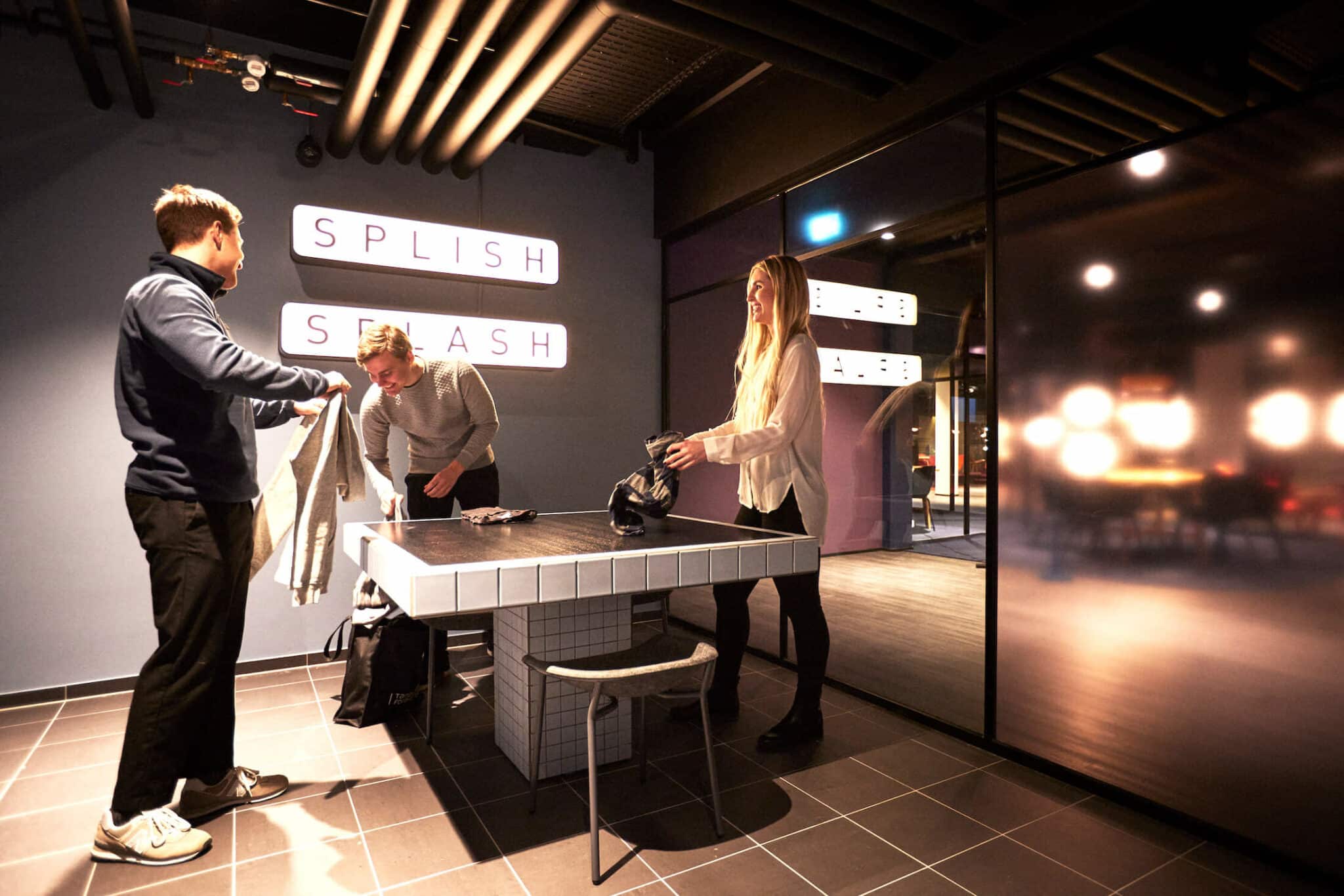 three young people fold their clothes at the Laundry zone of Baescamp Copenhagen student dormitory