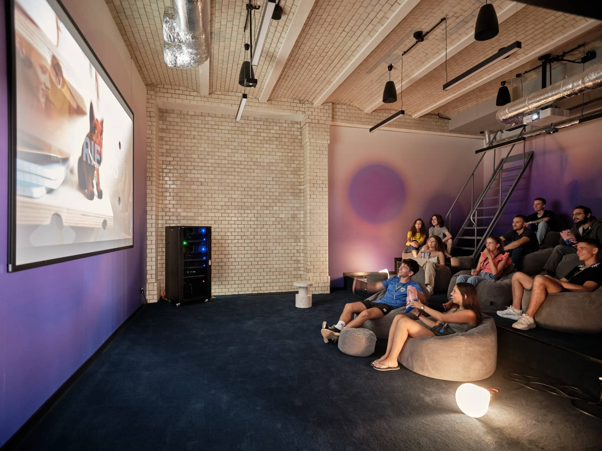 A group of students watch a movie and eat popcorn in the Cinema Room at Basecamp Wroclaw dorm