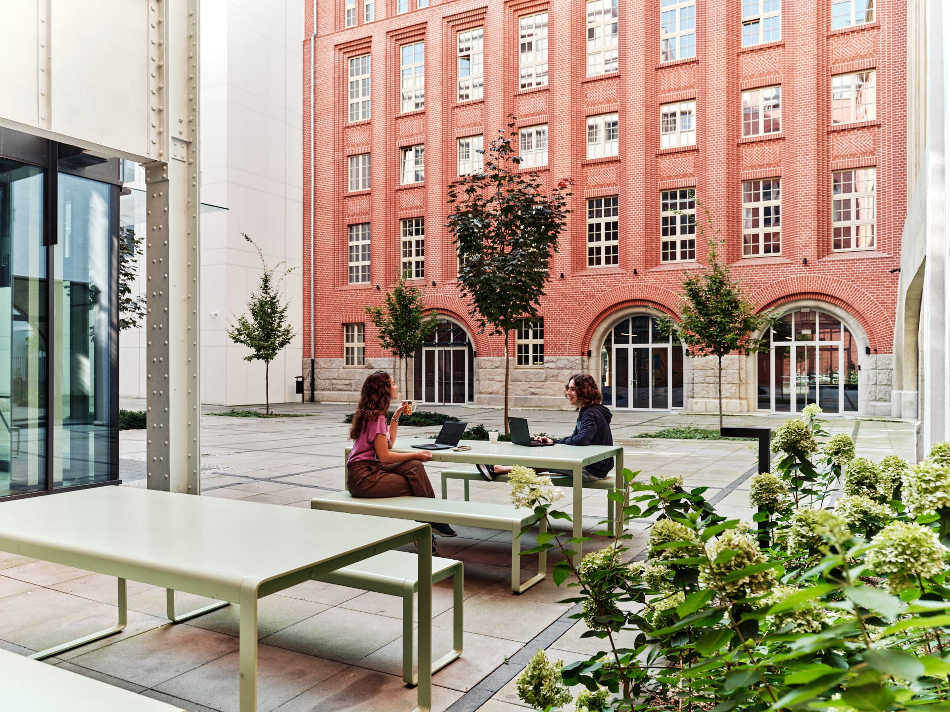 Two students working with their laptops at the Outdoor area of Basecamp Wroclaw student dormitory